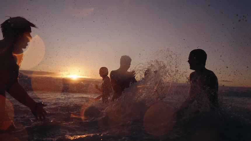 People play in the water at sunset creating silhouettes against the light