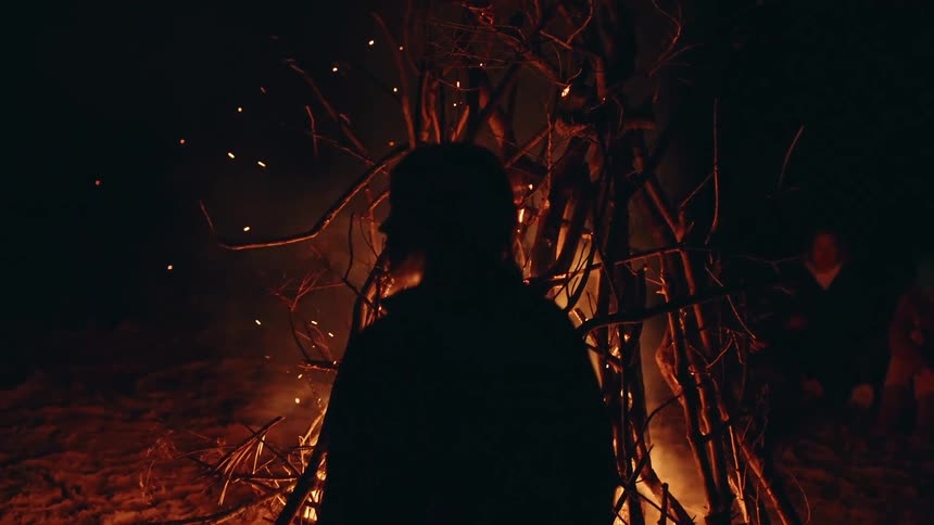 Silhouette of a teenager standing near a bonfire at night