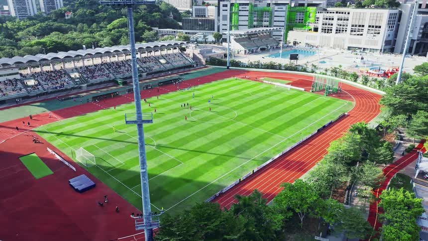 This is a highangle aerial shot of an outdoor stadium featuring a striped green soccer or football field surrounded by a reddishbrown running track scattered figures likely players are visible on the field