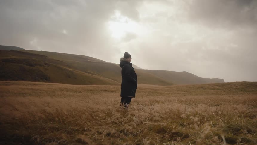 A person stands in a wide field of tall golden grass beneath a bright overcast sky