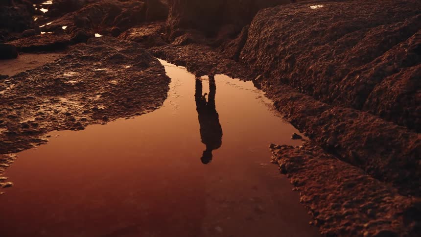 A silouette of a man reflected off a puddle at sunset