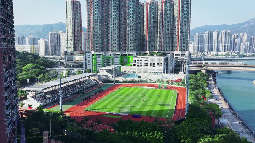 A tall building stands next to a soccer stadium and city skyline along a river