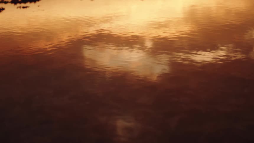A close view of a dark body of water reflecting the brilliant orange and yellow glow of a sunset