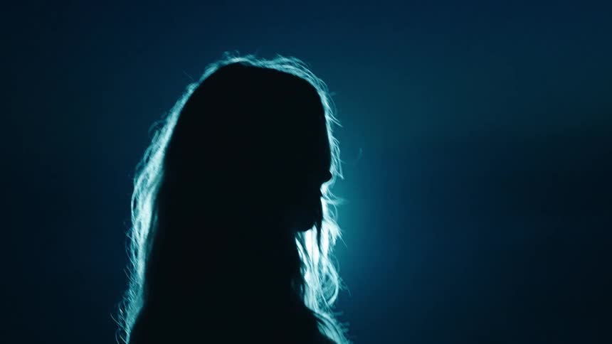 Backlit silhouette with blue light highlighting hair and head contours against dark background