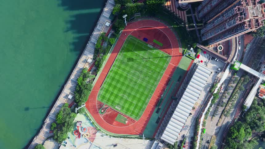 A stadium sits by the coast in the city featuring a football pitch illuminated by midday sunlight