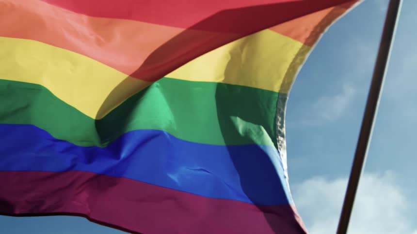 A colorful rainbow pattern flag is being waved under a blue sky