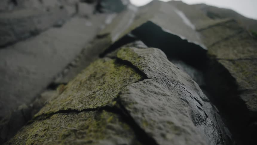 The video offers an extreme lowangle closeup perspective of a rough sheer rock face covered in patches of moss and moisture the camera emphasizes the immense verticality and jagged structure of the cliff or large boulders against a bright overcast