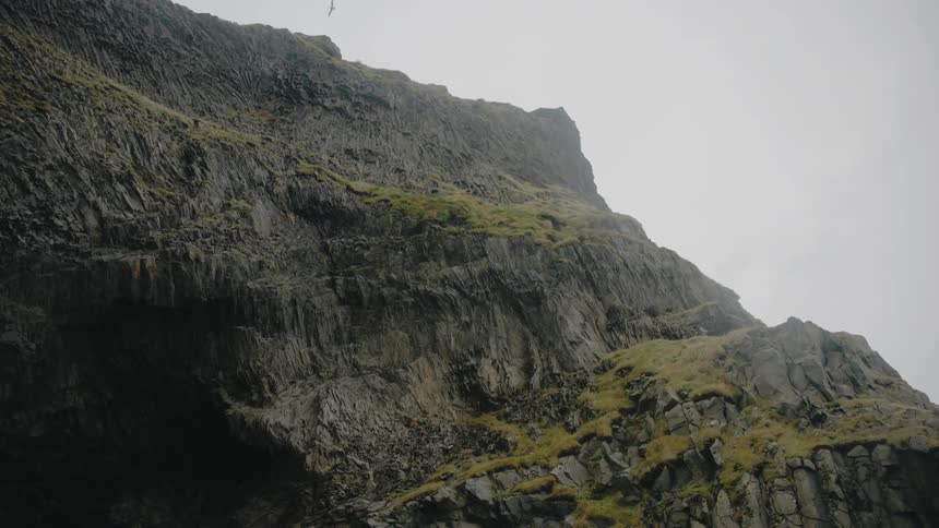Bird flies over the rough terrain of a mountain under a cloudy sky