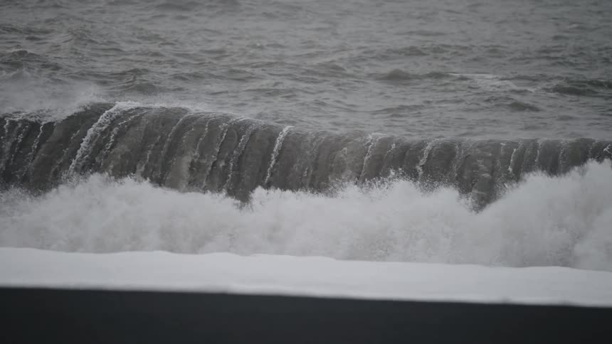 Rough water foams as it rolls into shore and splashes against the dock along the coast