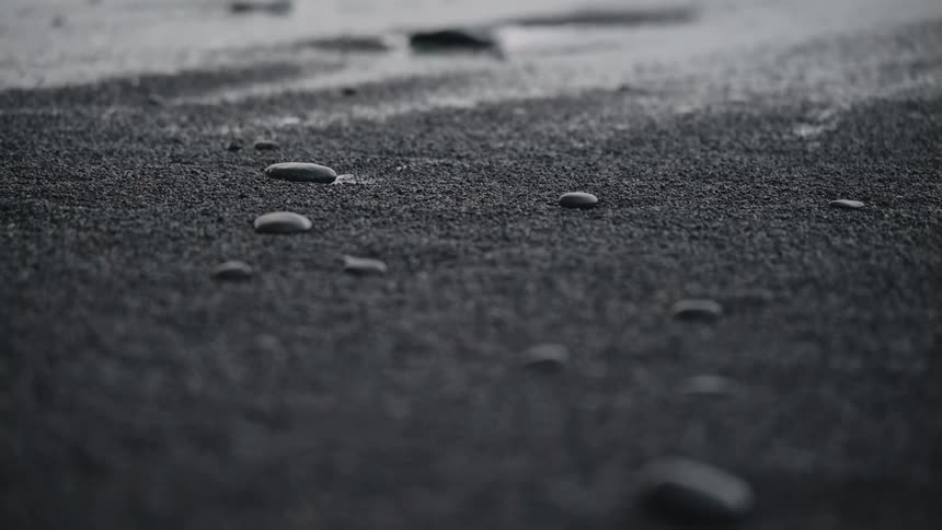 Close up of black smooth pebbles on shoreline of black sand beach
