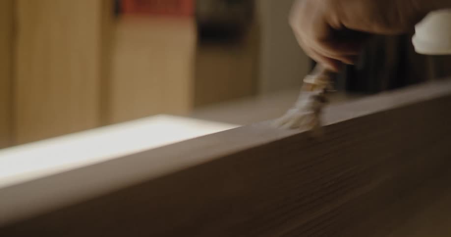 Closeup of a hand brushing finish onto a light wooden surface in a workshop