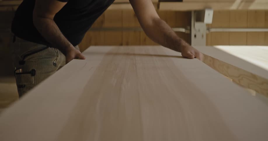 This closeup video shows a person in a workshop or studio working with long smooth wooden planksthe individual is carefully positioning and aligning two lightcolored wood pieces sidebyside likely preparing them for assembly into a larger surface