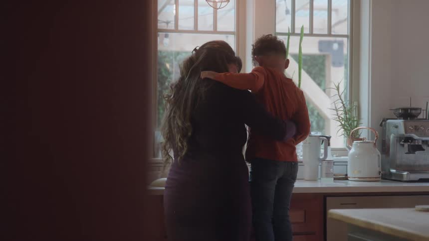 A mother kisses and embraces her young son in a bright kitchen