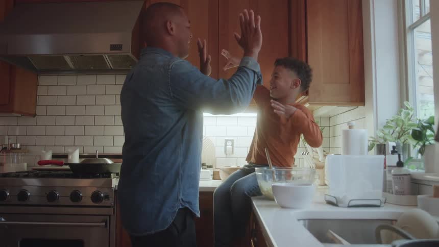 A man and a young boy smiling highfive each other in a warm kitchen