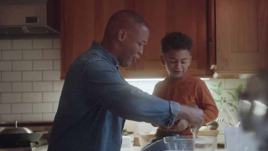 Father and son crack eggs into a glass bowl while preparing food together in a modern kitchen
