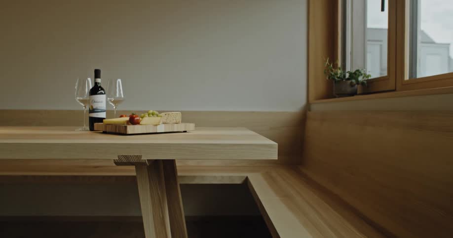 A dining table at midday holds two wine glasses a bottle of wine and a plate of food resting neatly in place