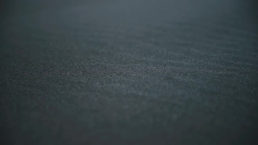 The video shows a closeup static shot of a dark subtly textured surface possibly black sand asphalt or a synthetic materialthe texture consists of fine uniformly distributed grains creating a slightly rough matte finish across the entire fram