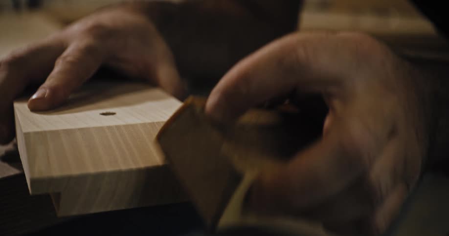 A closeup video shows a persons hands sanding the end of a piece of lightcolored wood the wood appears to be part of a woodworking project featuring a joint or rabbet cut at the end