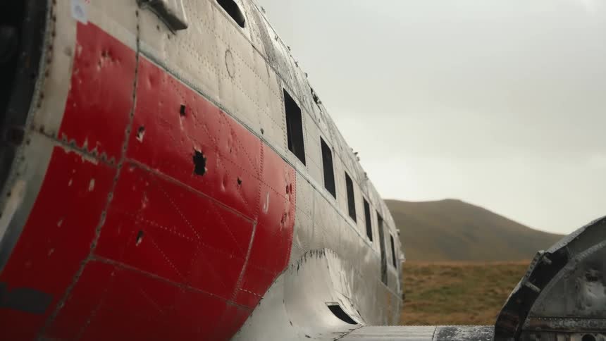 A damaged red and silver airplane fuselage resting in a grassy landscape