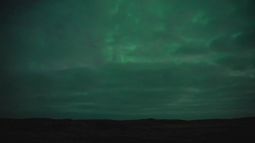 Night sky displaying green auroras over a dark landscape