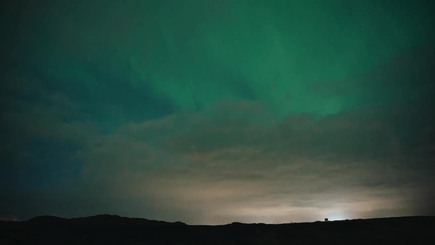 Northern lights of the aurora borealis glow in the sky above the clouds