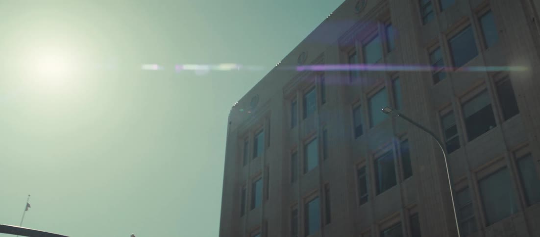 A lowangle panning shot sweeps quickly from an ornate white skyscraper across the bright sun to reveal a neighboring brick building