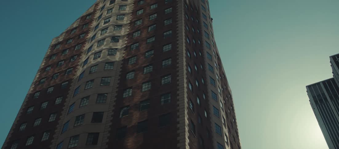 A low angle shot looks up at a tall older brick apartment building with many windows against a clear blue sky