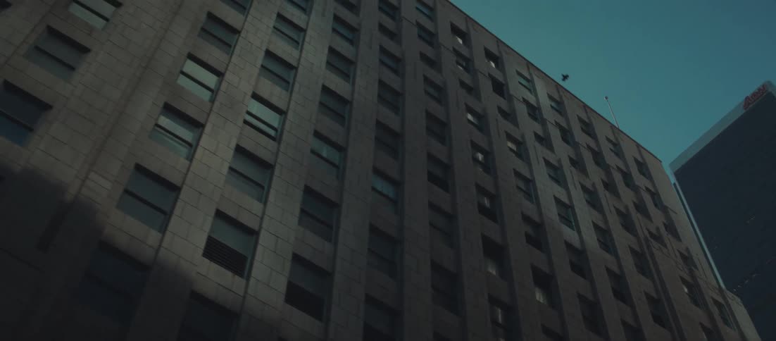This video clip is a slow upward panning shot that reveals the facade of a tall historic urban buildingthe structure features many rows of rectangular windows dark grey stone or concrete cladding and a reddish brick section towards the end of the