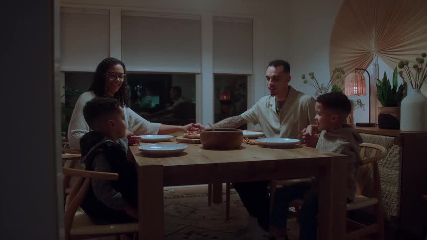 A family holds hands to pray before they eat the pizza on the table