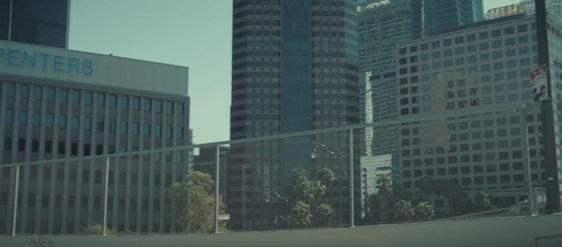 A sunny view of skyscrapers and palm trees is seen from a highway overpass