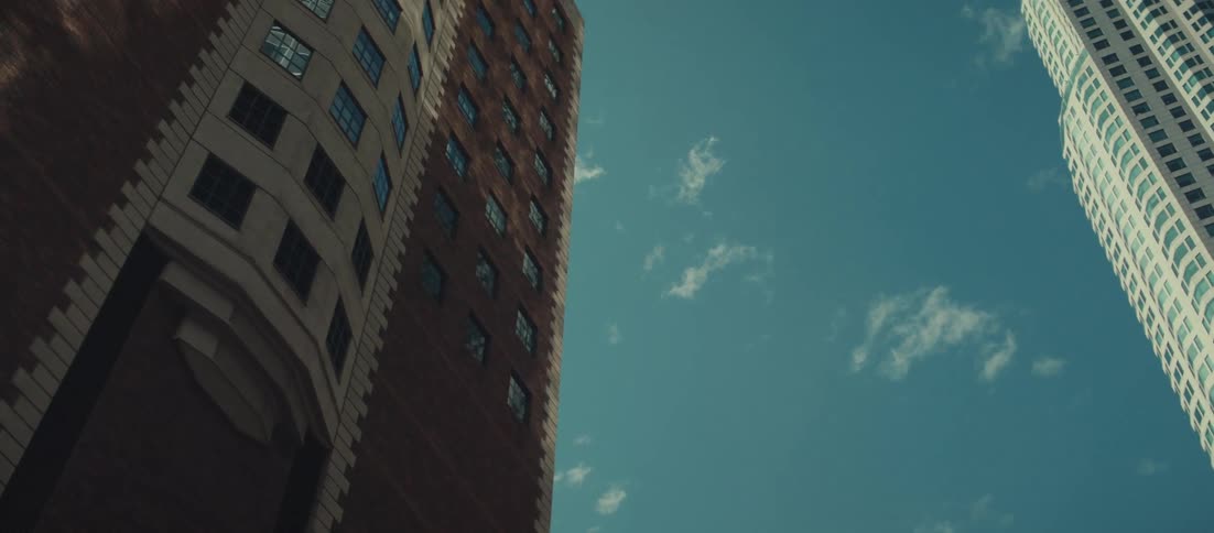 A city view on a sunny day shows a series of skyscrapers towering overhead seen from the ground looking up