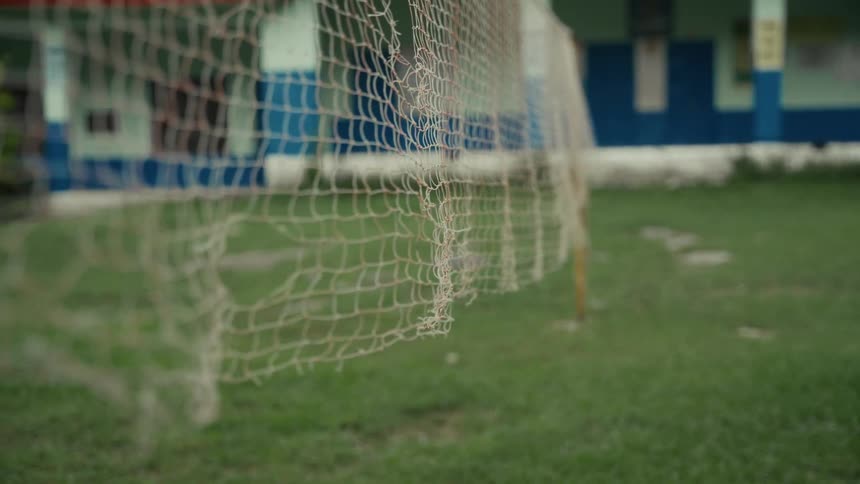 A torn net stretches across grass in front of a building