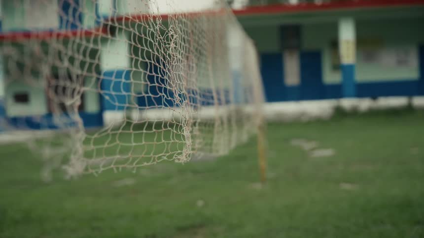 Ripped netting blows in the wind on a field located near a school building on a summer day