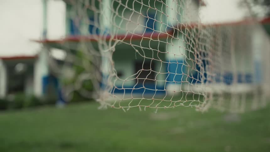 Worn goal net appears in the foreground on a school grass field