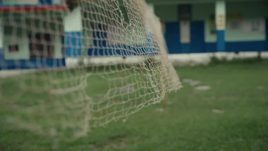A handheld closeup shot focuses on the white mesh of a soccer goal net gently swaying above a green grassy field