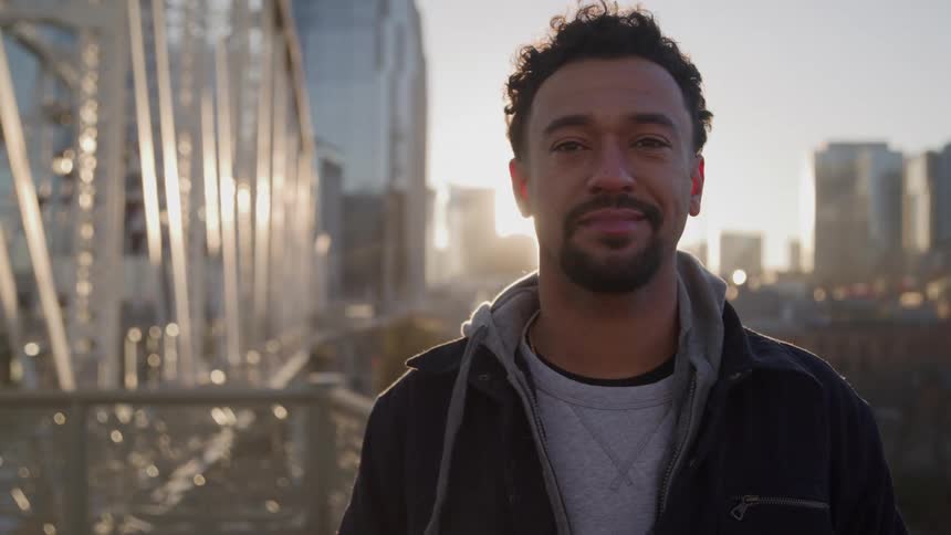 A man is standing on a bridge that leads out of a city