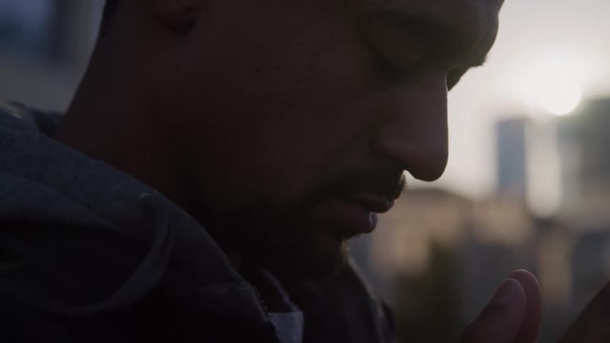 A mans profile is shown as he has his eyes closed head down and and his hands are in a prayer position