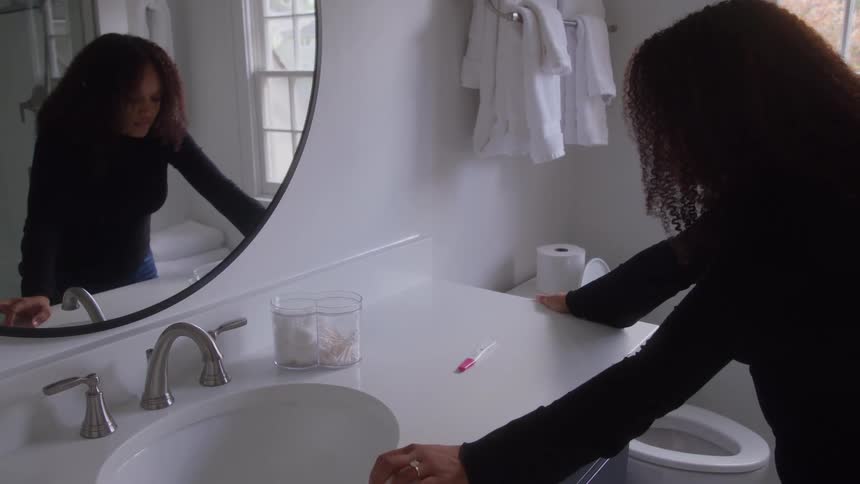 Woman leans on the bathroom sink while looking at a pregnancy test on the counter