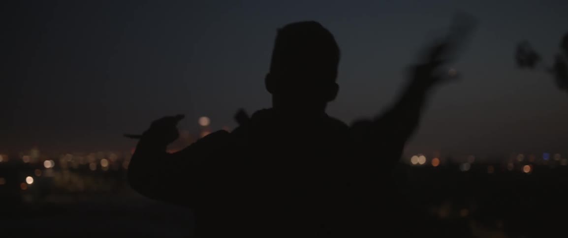 A man throws a rock at night with city lights in the distance