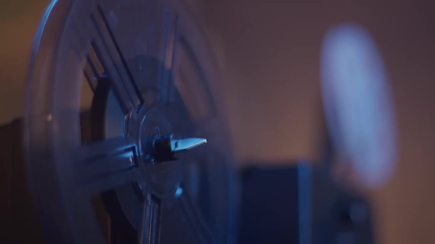 An old film projector reel spins inside a room its motion casting a nostalgic atmosphere