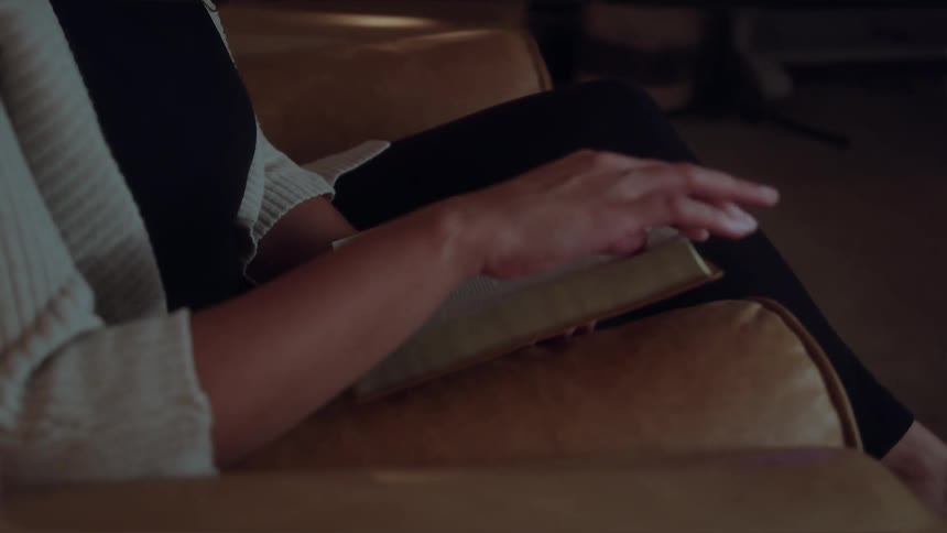 A woman sits in an armchair flipping through the pages of a bible as she reads