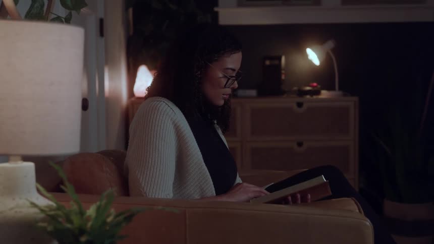 A woman reading a book on a brown leather chair in a cozy dimly lit room