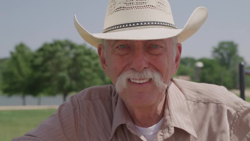 Smiling man wearing a cowboy hat poses outdoors on a sunny day