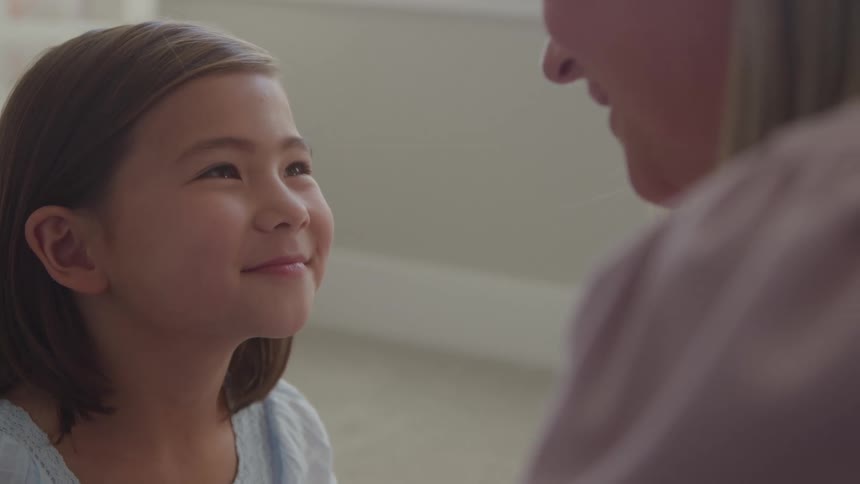 The video is a closeup profile shot of a young girl looking up and smiling warmly at an adult whose shoulder and chin are visible in the right foregroundthe girl has light brown hair and a bright genuine expression suggesting a happy and engaging c