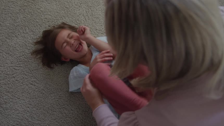 Grandaughter laying on carpet laughing being tickled by her grandmother