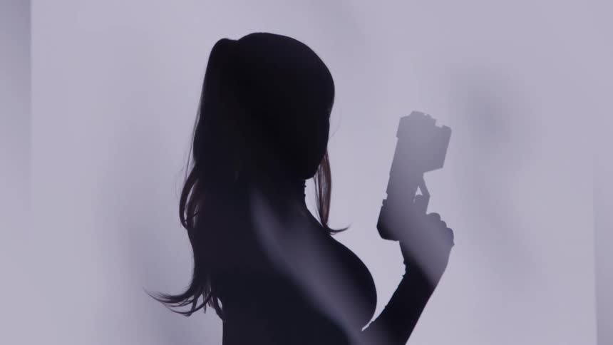 Female silhouette holds a gun pointed upward against a bright background