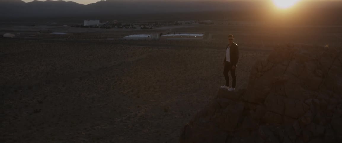 A man stands on a rocky ledge as the sun sets