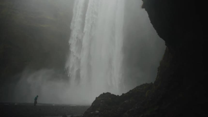 A person walks toward a waterfall in the mountains at midday