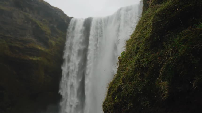 Massive waterfall flowing down mossy canyon in slow motion