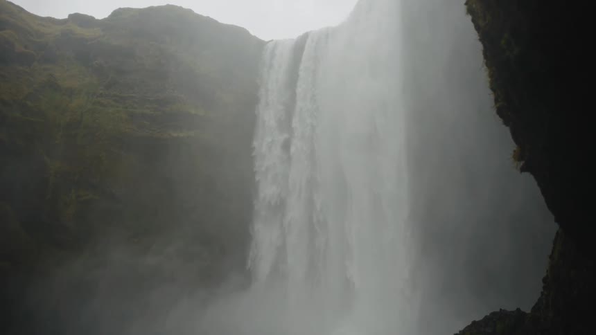 A very large waterfall with mist obscuring much of the top and surrounding landscape the water is white and powerful falling between steep dark mosscovered cliffs
